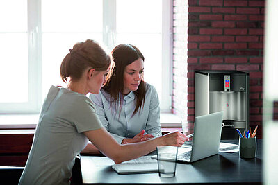 Zwei Frauen bei der Arbeit mit Wasserspender im Büro