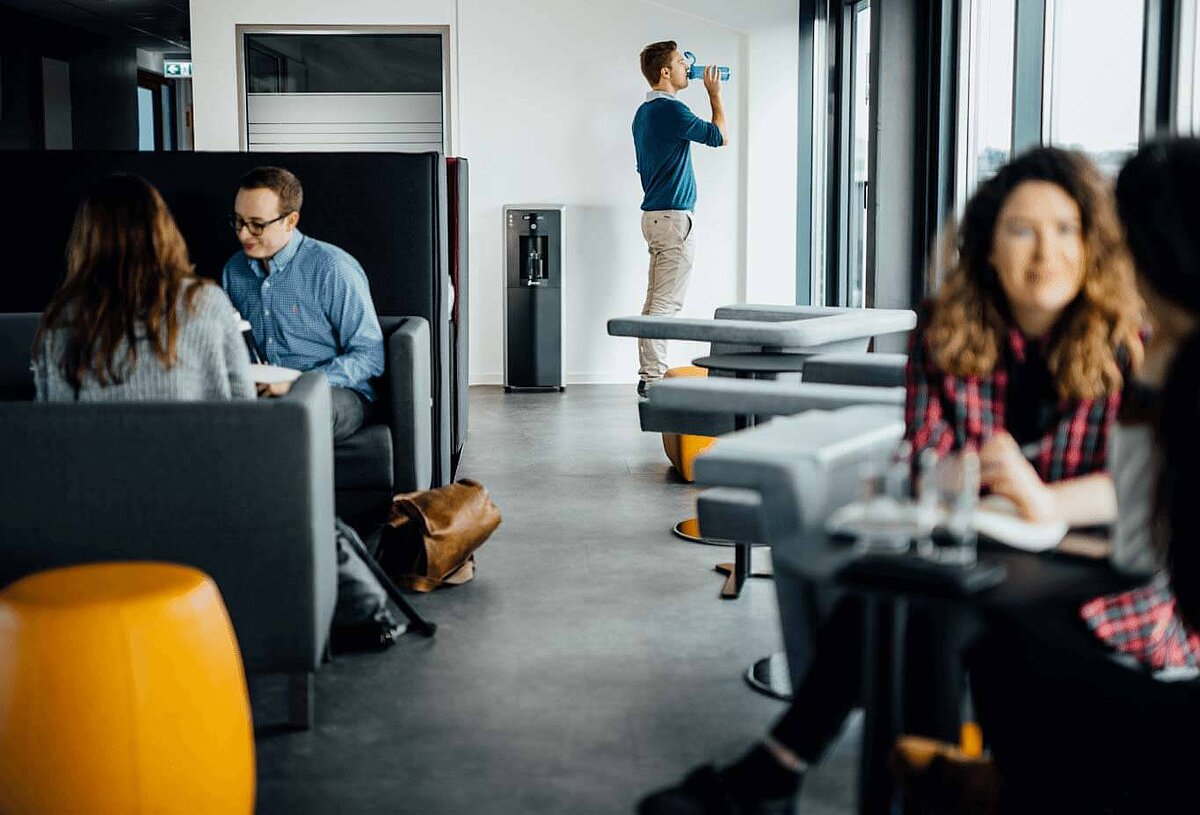 Offener Arbeitsraum mit Personen in Gesprächen und trinkenden Mann und Waterlogic Wasserspender im Hintergrund           