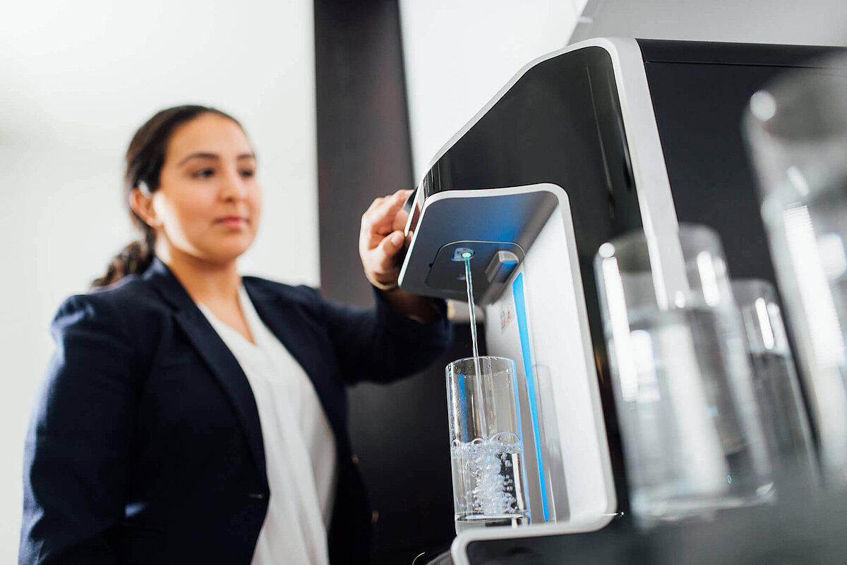 Frau erhält sprudelndes Wasser an Festwasserspender