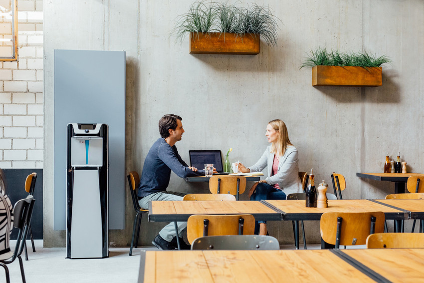Zwei Personen unterhalten sich in einer modernen Kantine wo ein Waterlogic WL7 Wasserspender steht 