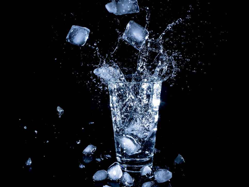 Eiswürfel fallen in ein volles Wasserglas      